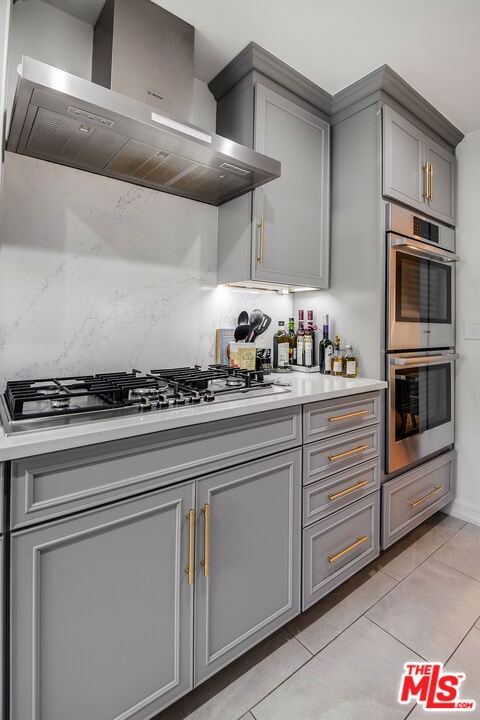 kitchen featuring decorative backsplash, appliances with stainless steel finishes, gray cabinetry, and wall chimney range hood