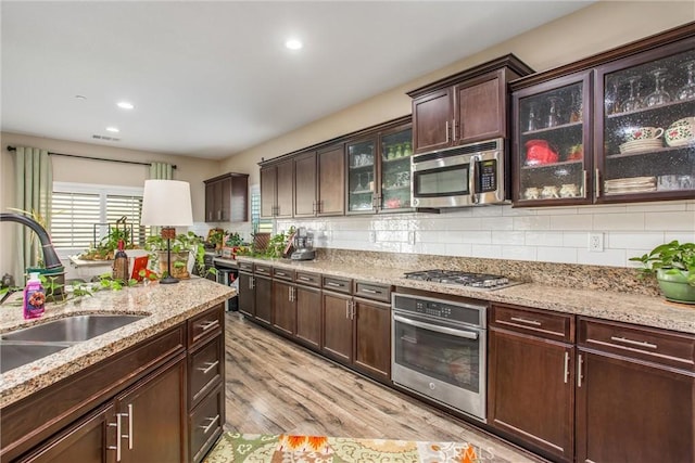 kitchen featuring sink, light hardwood / wood-style flooring, stainless steel appliances, light stone counters, and decorative backsplash