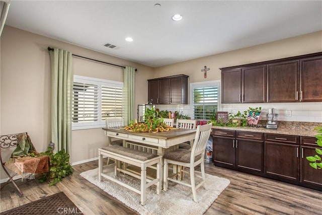 kitchen with dark brown cabinetry, backsplash, light hardwood / wood-style floors, and light stone countertops