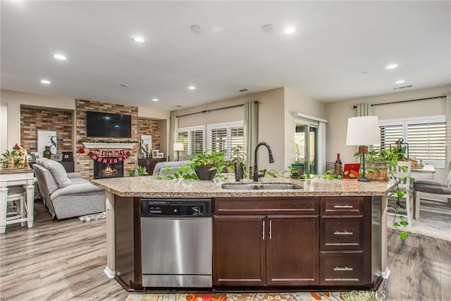 kitchen with stainless steel dishwasher, an island with sink, a fireplace, and sink