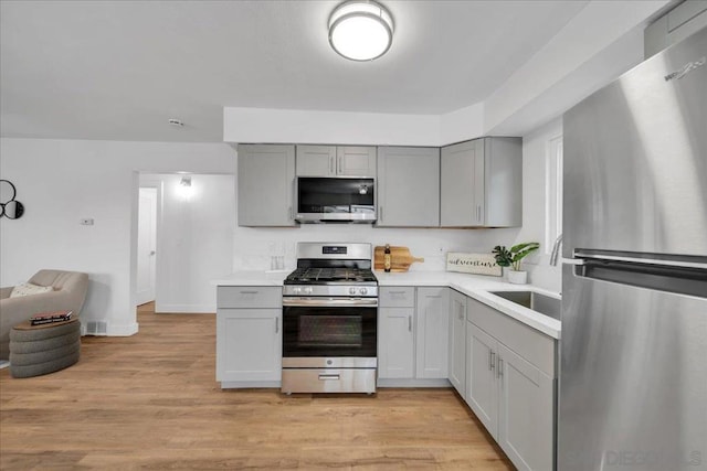 kitchen with appliances with stainless steel finishes, gray cabinetry, and light hardwood / wood-style floors