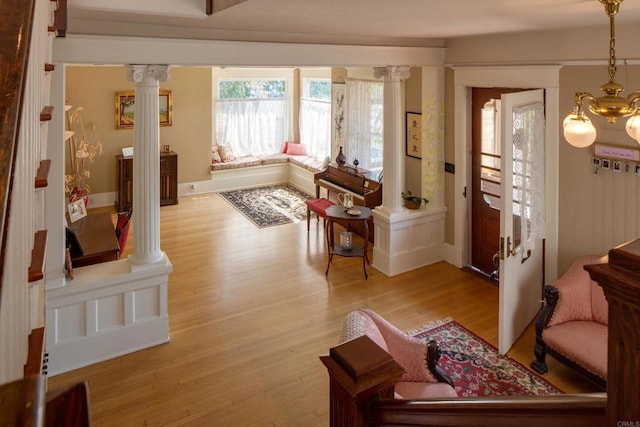 living area with ornate columns, a notable chandelier, and light wood-type flooring