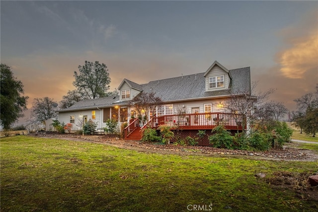 back house at dusk featuring a lawn and a wooden deck