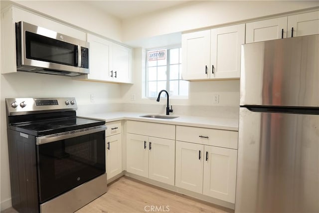 kitchen with sink, white cabinets, appliances with stainless steel finishes, and light hardwood / wood-style flooring