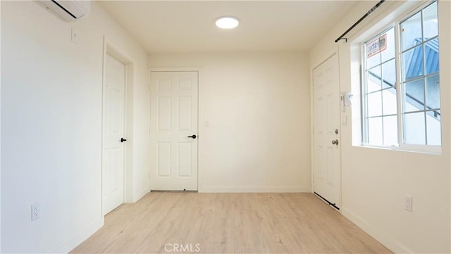 interior space featuring a healthy amount of sunlight, light wood-type flooring, and a wall mounted air conditioner