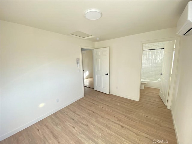 unfurnished bedroom featuring a wall unit AC, connected bathroom, and light wood-type flooring