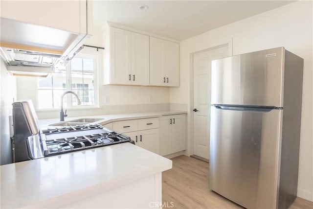 kitchen with white cabinetry, stainless steel fridge, gas range oven, light hardwood / wood-style flooring, and sink