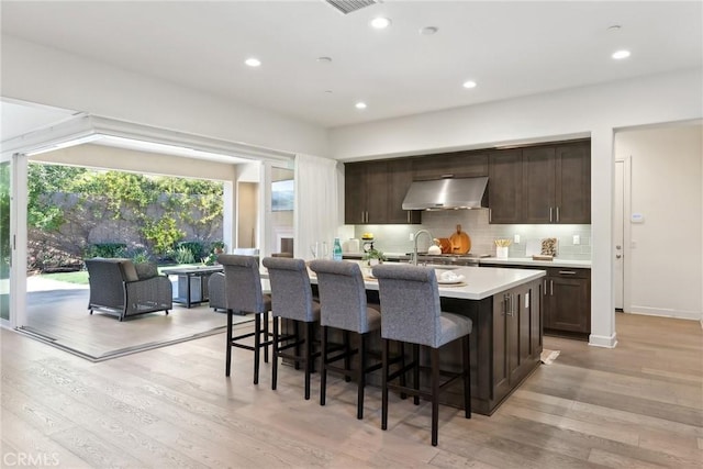 kitchen with a kitchen island with sink, a kitchen bar, range hood, and light wood-type flooring