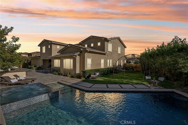 back house at dusk with a swimming pool with hot tub, a patio area, a lawn, and a water view