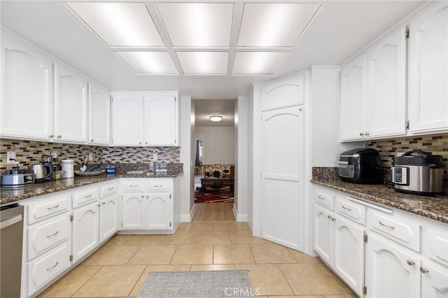 kitchen with tasteful backsplash, light tile patterned flooring, dark stone countertops, stainless steel dishwasher, and white cabinets