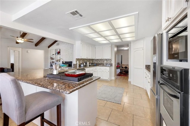 kitchen with a breakfast bar area, appliances with stainless steel finishes, tasteful backsplash, dark stone countertops, and white cabinets