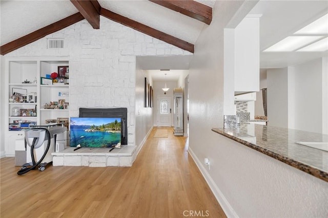 living room featuring built in features, light hardwood / wood-style flooring, lofted ceiling with beams, and a stone fireplace