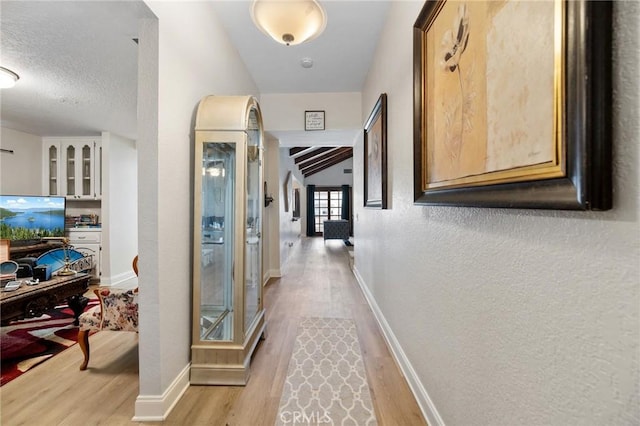 hallway with light wood-type flooring, vaulted ceiling, and a textured ceiling