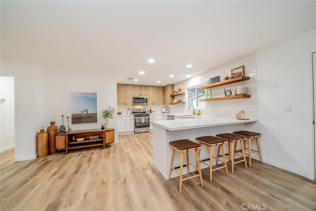 kitchen with a kitchen bar, stainless steel appliances, light hardwood / wood-style floors, sink, and kitchen peninsula