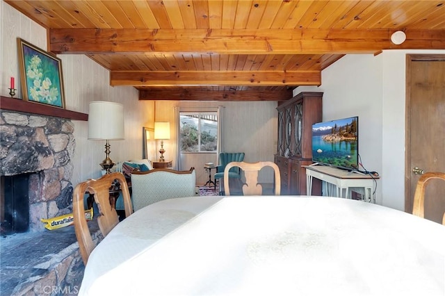 dining space featuring wood ceiling, beamed ceiling, and a stone fireplace