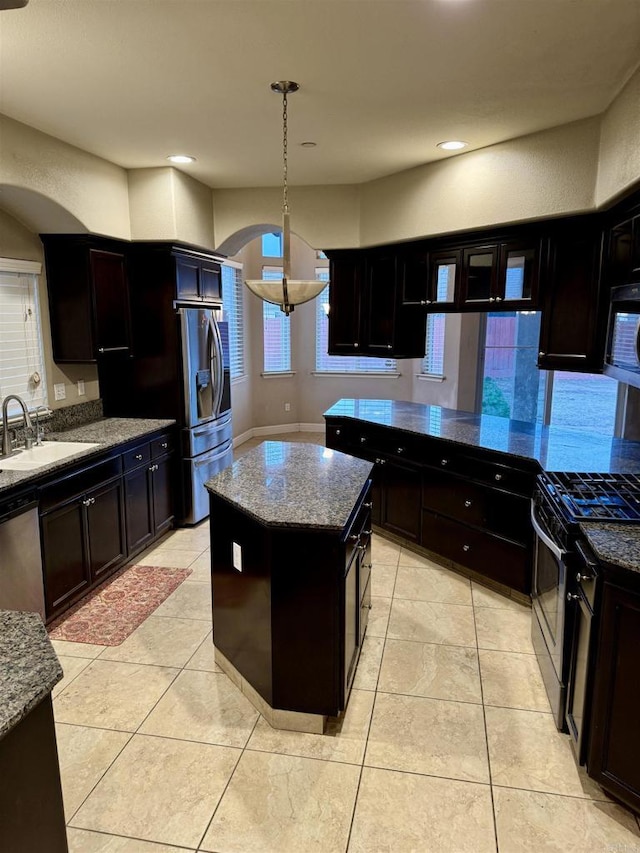 kitchen featuring light stone countertops, appliances with stainless steel finishes, a center island, sink, and dark brown cabinets