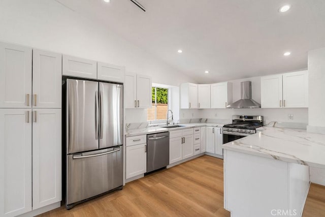 kitchen with kitchen peninsula, wall chimney range hood, stainless steel appliances, and white cabinetry