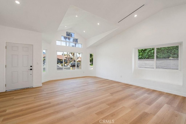 unfurnished living room with high vaulted ceiling, light wood-type flooring, and plenty of natural light