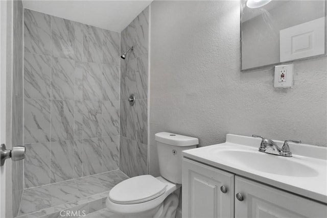 bathroom with toilet, tiled shower, and vanity