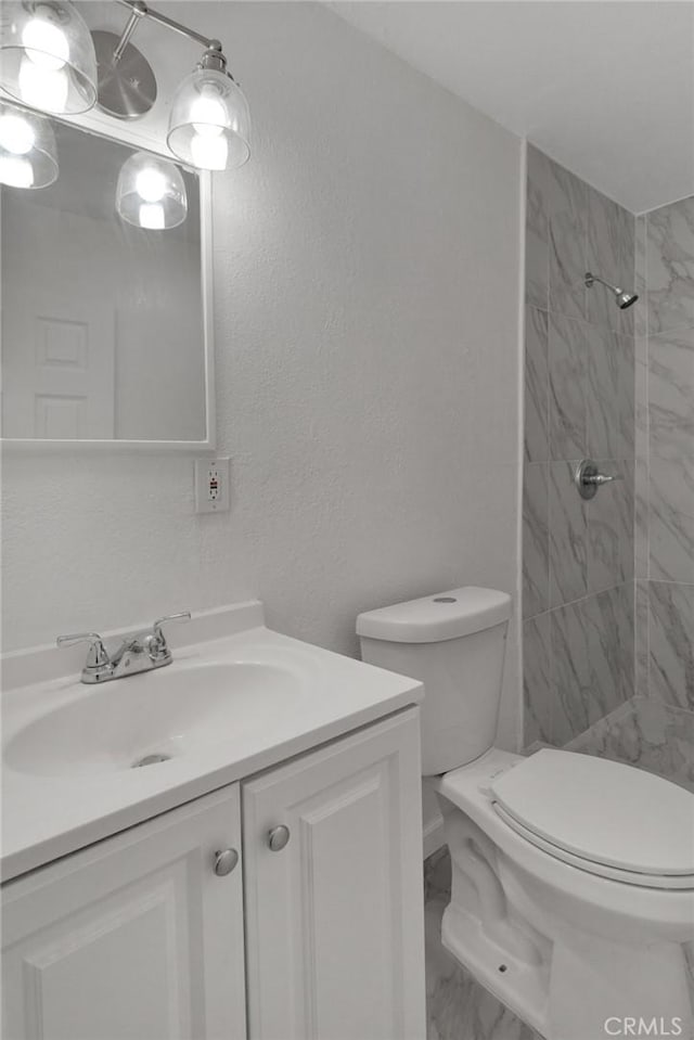 bathroom featuring toilet, tiled shower, and vanity