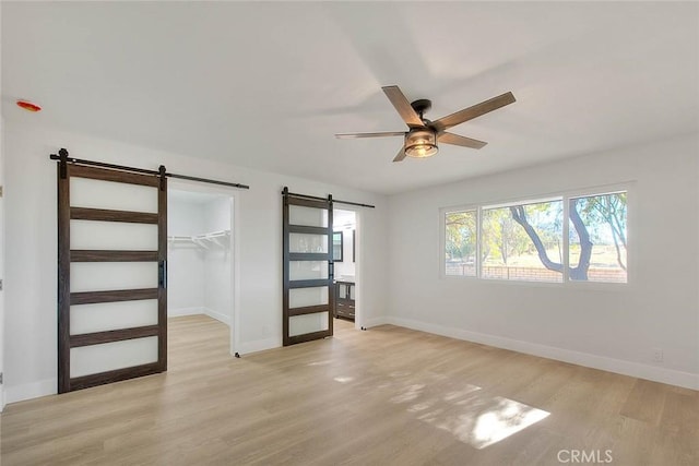 unfurnished bedroom with ceiling fan, a barn door, a closet, and light hardwood / wood-style floors