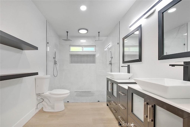 bathroom featuring toilet, vanity, wood-type flooring, and a tile shower