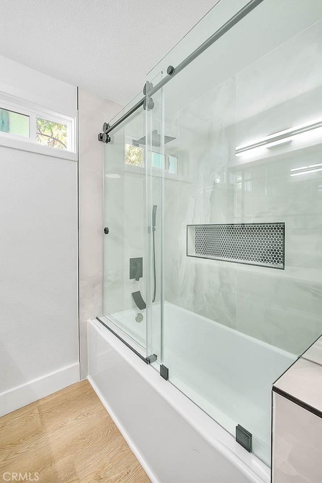 bathroom featuring hardwood / wood-style floors, shower / bath combination with glass door, and a textured ceiling