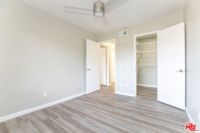 unfurnished bedroom with a closet, a walk in closet, light hardwood / wood-style floors, and ceiling fan