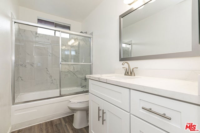 full bathroom featuring hardwood / wood-style flooring, vanity, toilet, and bath / shower combo with glass door