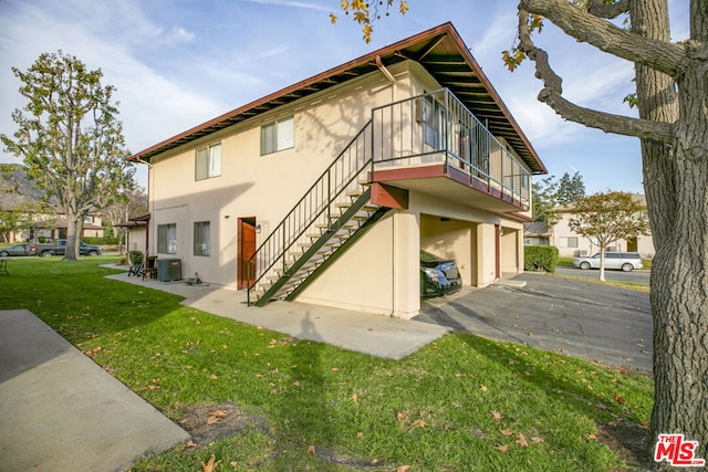 rear view of property featuring a garage, central AC unit, and a lawn