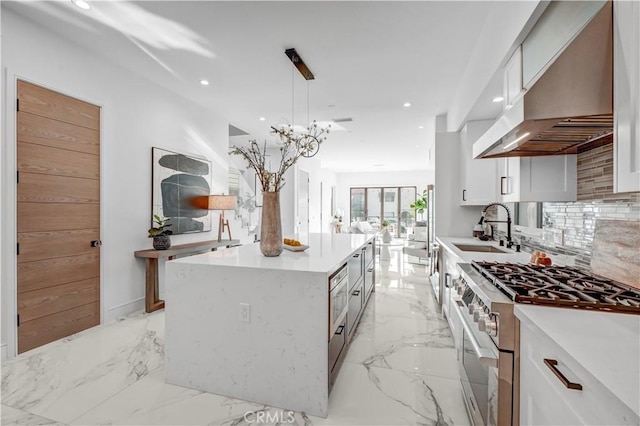 kitchen featuring wall chimney exhaust hood, stainless steel stove, white cabinetry, and a kitchen island