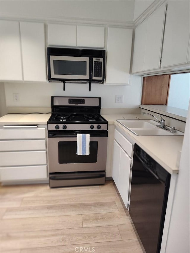 kitchen featuring stainless steel gas range oven, sink, black dishwasher, white cabinetry, and light wood-type flooring