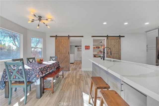 kitchen featuring light wood-type flooring, light stone countertops, a barn door, and sink