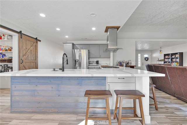 kitchen with a barn door, stainless steel fridge, island exhaust hood, gray cabinetry, and sink