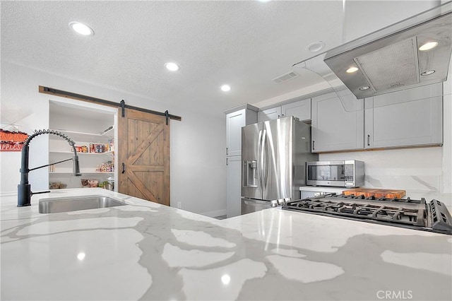 kitchen featuring stainless steel appliances, sink, gray cabinets, light stone counters, and a barn door