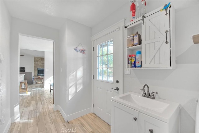 clothes washing area with a fireplace, light hardwood / wood-style floors, and sink