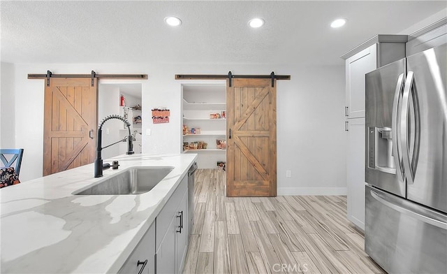 kitchen featuring light stone counters, sink, appliances with stainless steel finishes, and a barn door