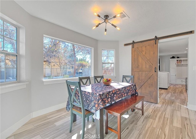 dining space featuring light hardwood / wood-style floors, a barn door, and a notable chandelier