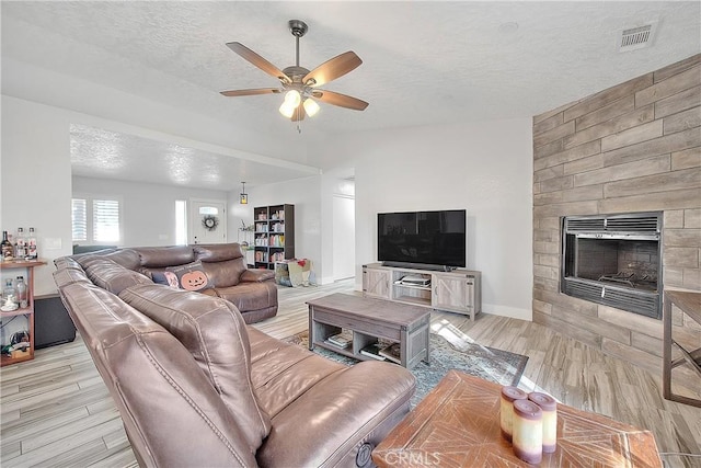 living room with ceiling fan, a large fireplace, and a textured ceiling