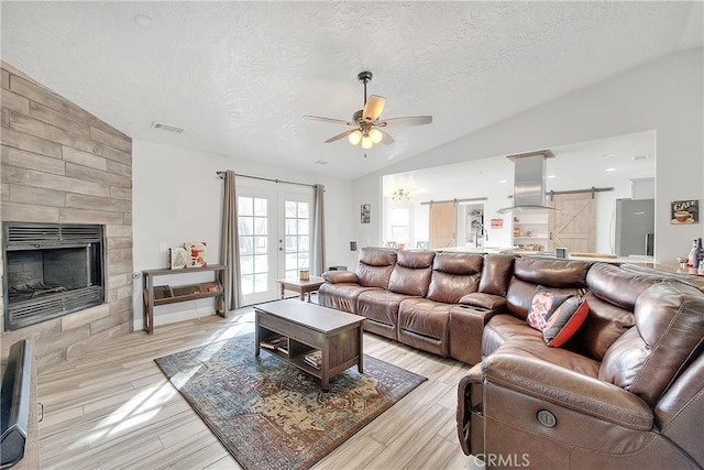 living room featuring lofted ceiling, a barn door, ceiling fan, and a textured ceiling