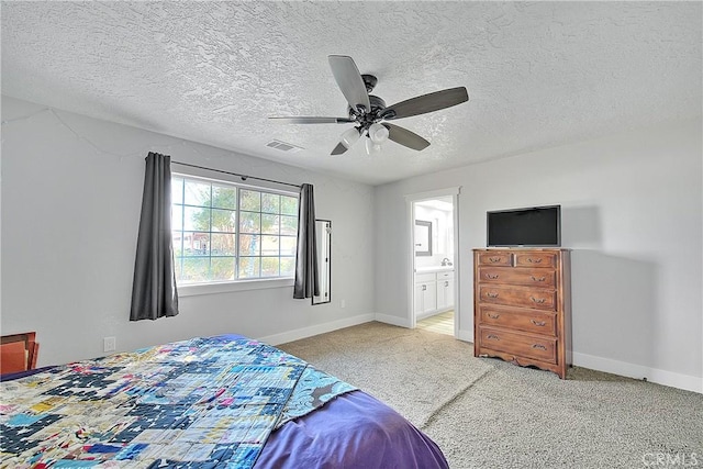 bedroom featuring ceiling fan, ensuite bath, carpet floors, and a textured ceiling