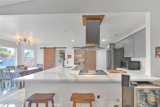 kitchen with kitchen peninsula, gray cabinets, island range hood, and a barn door