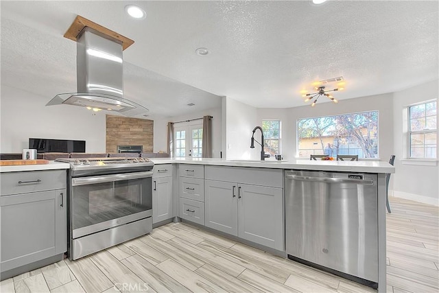 kitchen with kitchen peninsula, appliances with stainless steel finishes, island range hood, and gray cabinetry