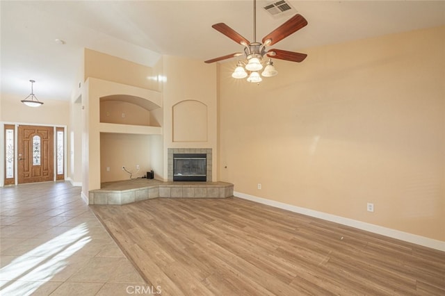 unfurnished living room with ceiling fan, light tile patterned flooring, a towering ceiling, and a fireplace