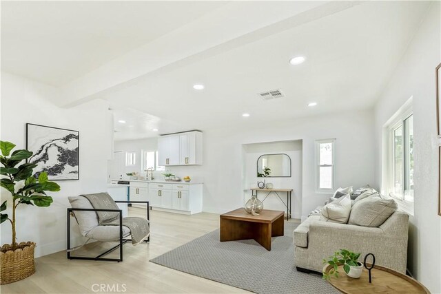 living room featuring light hardwood / wood-style floors, sink, and beamed ceiling