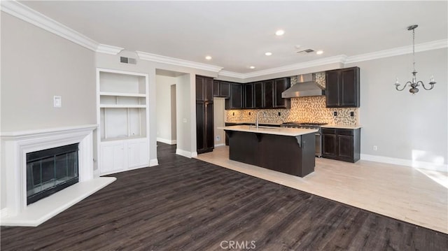 kitchen with hardwood / wood-style floors, wall chimney exhaust hood, built in shelves, a center island with sink, and a breakfast bar area