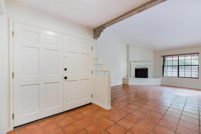 entryway featuring light tile patterned floors, beam ceiling, and a fireplace