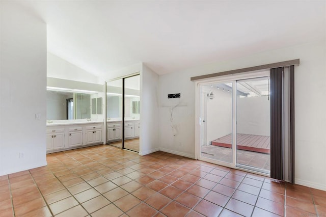 unfurnished bedroom featuring vaulted ceiling, a closet, light tile patterned floors, and connected bathroom