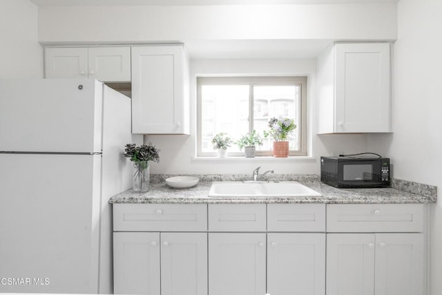 kitchen featuring light stone countertops, sink, white cabinetry, and white fridge