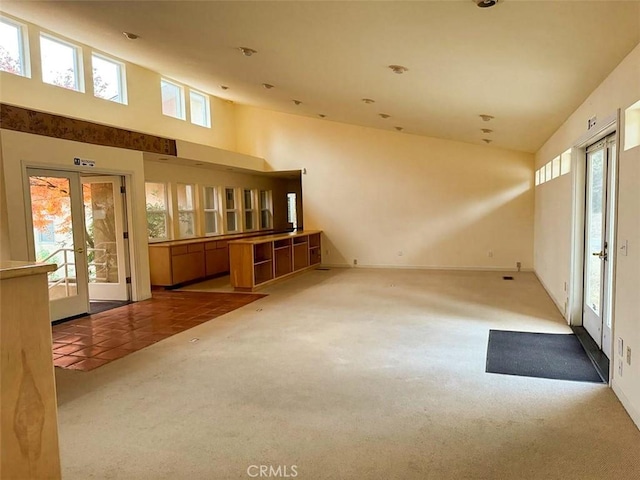 carpeted empty room featuring plenty of natural light, a towering ceiling, and french doors